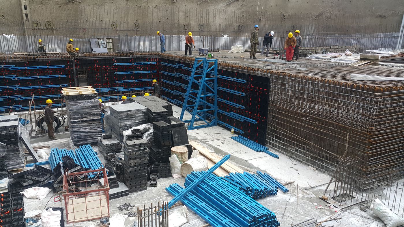 Workers in hard hats at a basement construction site with wall formwork and rebar
