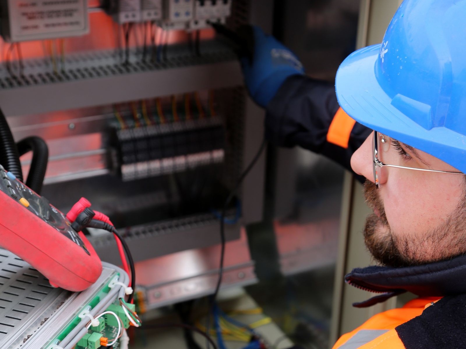 Electrician in a hard hat testing an electrical control panel with a multimeter