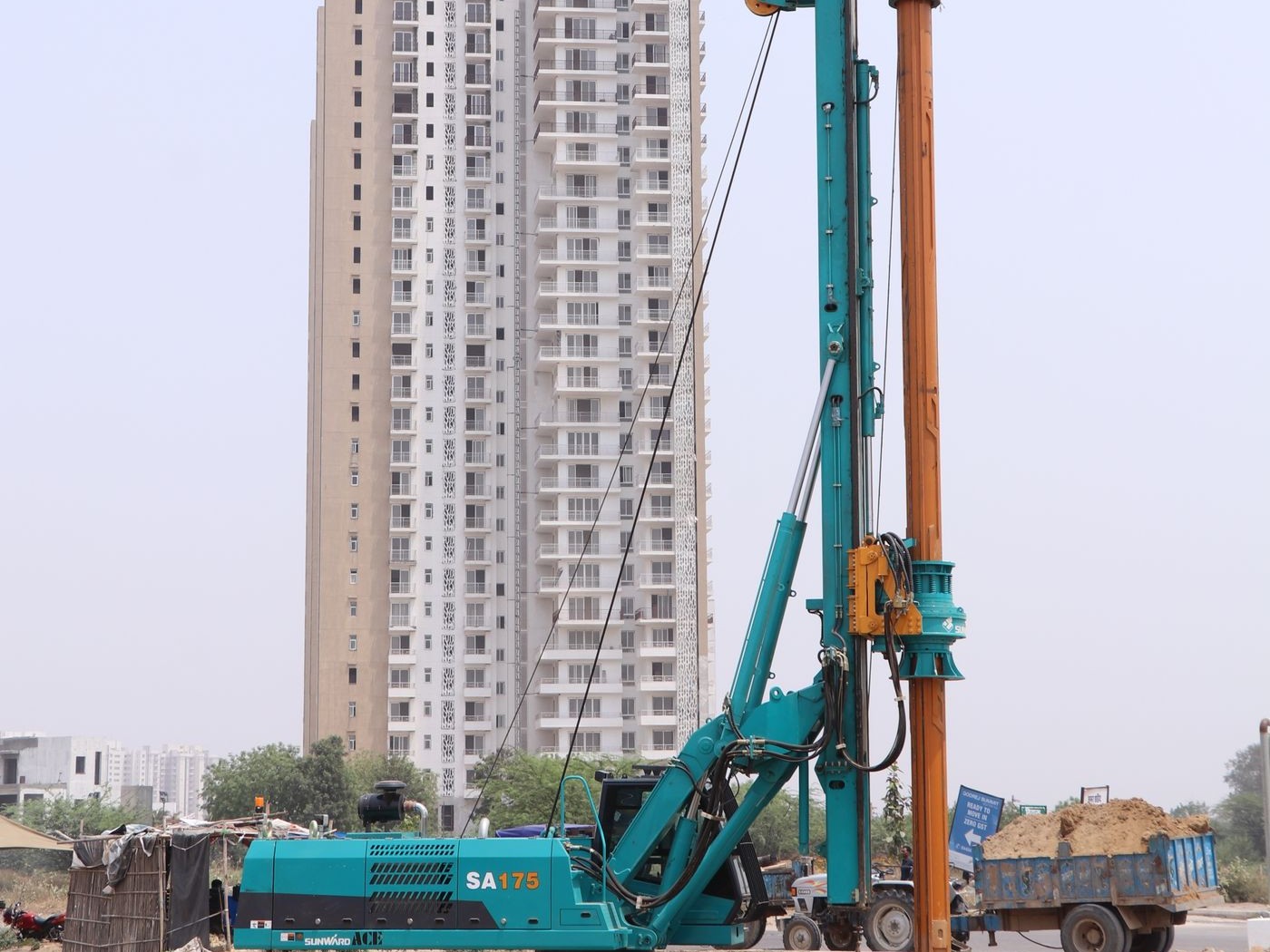 Rotary piling rig drilling a foundation pile next to a high-rise tower