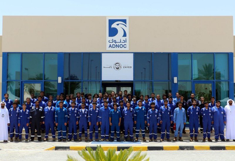 Workers in blue coveralls gathered in front of the ADNOC training center