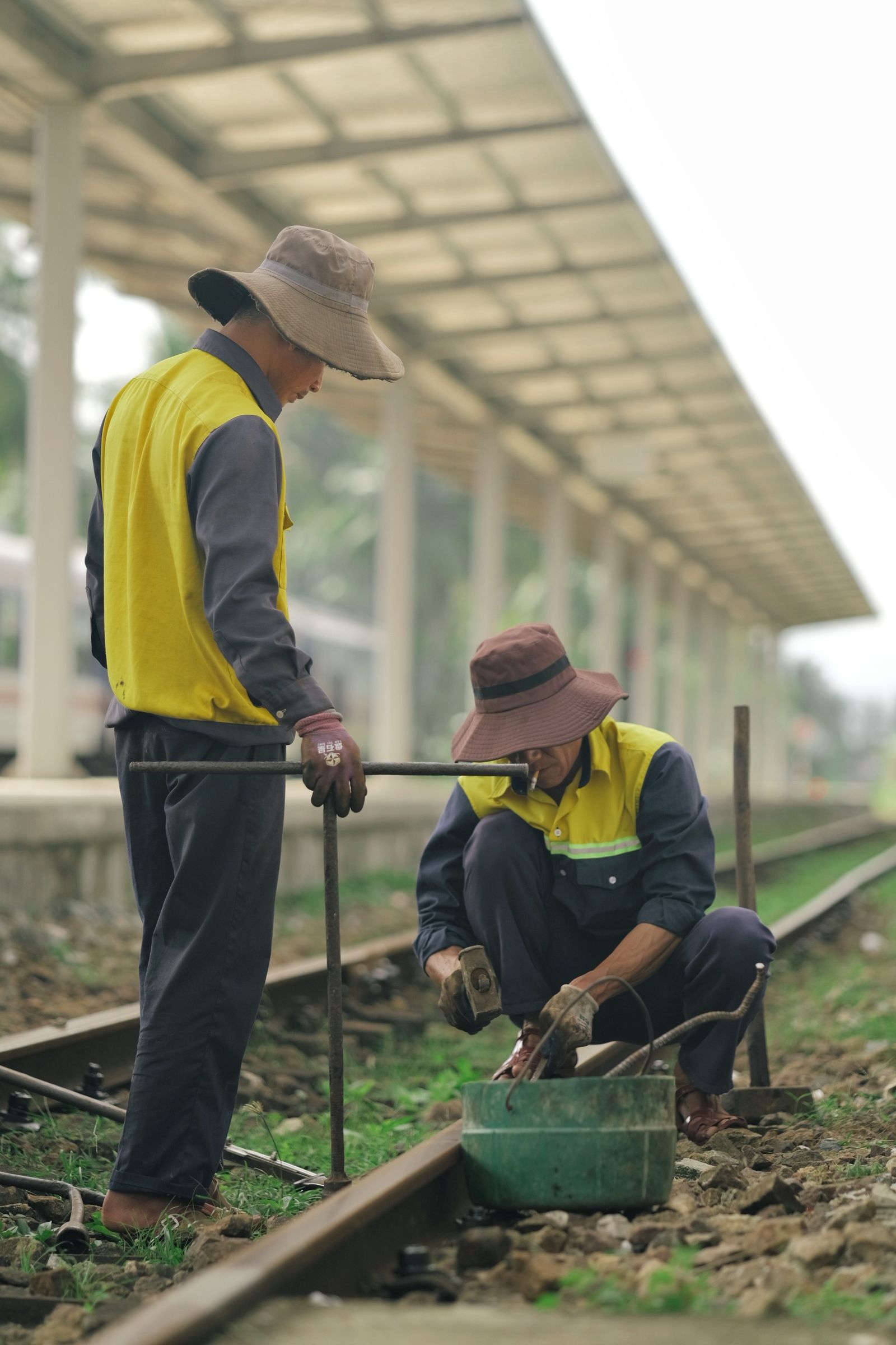 Two railway workers in yellow vests maintaining tracks outdoors