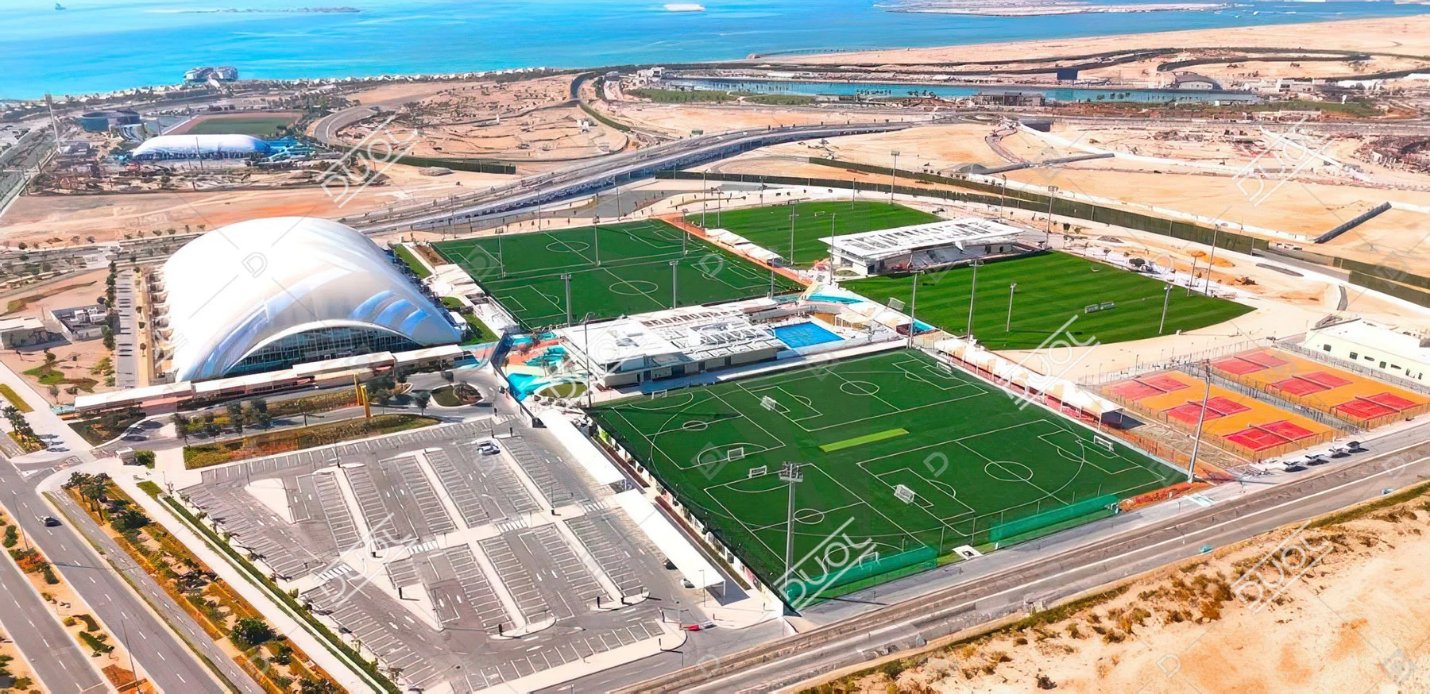 Aerial view of a sports complex with football pitches and a domed arena on Hudayriyat Island