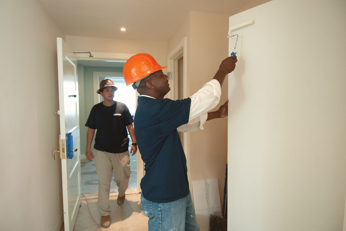 Painter in a hard hat rolling paint onto an interior wall